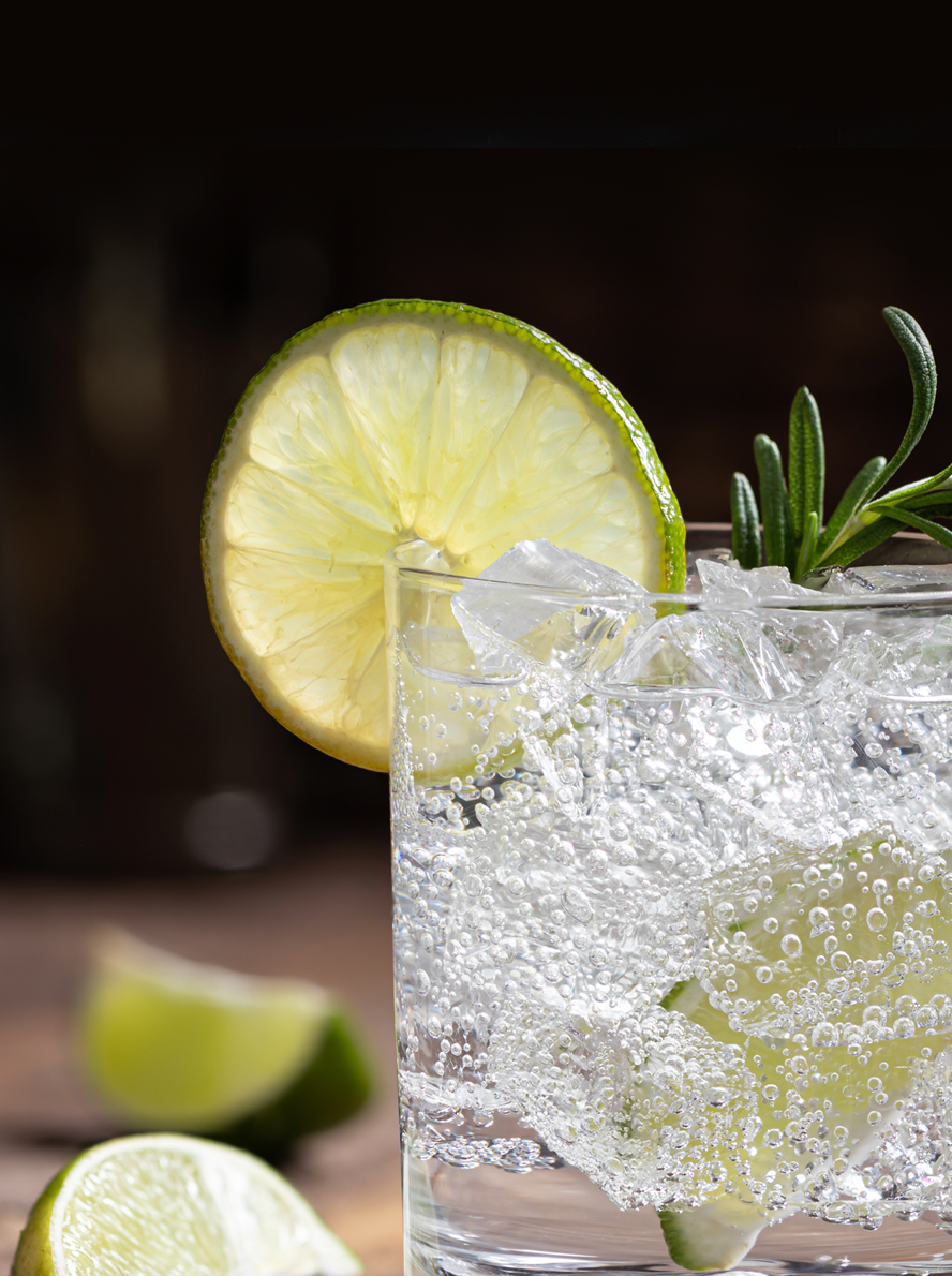 Glass of a sparkling beverage garnished with lime and rosemary.